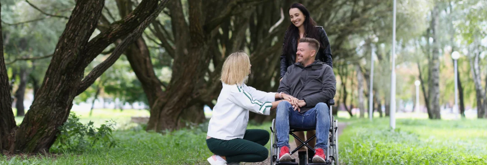 Support worker assisting a man in a wheelchair on a walk through a park